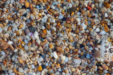 sahil arka plan taşları üzerinde deniz çakıl renkli granit. Kum ve çakıl taşlarıyla sahilin kıyısı deniz dalgalarıyla yıkanmış..