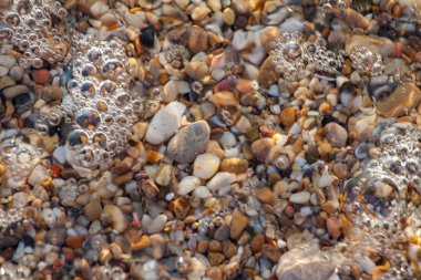 sahil arka plan taşları üzerinde deniz çakıl renkli granit. Kum ve çakıl taşlarıyla sahilin kıyısı deniz dalgalarıyla yıkanmış..