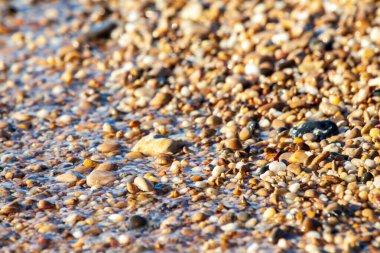 sahil arka plan taşları üzerinde deniz çakıl renkli granit. Kum ve çakıl taşlarıyla sahilin kıyısı deniz dalgalarıyla yıkanmış..