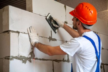 Usta ustabaşı bir ev inşa ederken havalandırmalı beton bloklardan bir duvar örer. Özel konut inşaatı. Havalı beton bloklar inşa etmek için modern teknoloji ve malzemeler.