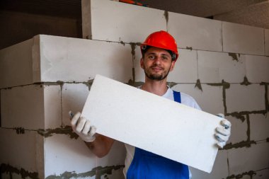 Usta ustabaşı bir ev inşa ederken havalandırmalı beton bloklardan bir duvar örer. Özel konut inşaatı. Havalı beton bloklar inşa etmek için modern teknoloji ve malzemeler.