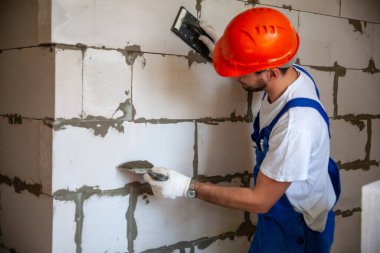 Usta ustabaşı bir ev inşa ederken havalandırmalı beton bloklardan bir duvar örer. Özel konut inşaatı. Havalı beton bloklar inşa etmek için modern teknoloji ve malzemeler.