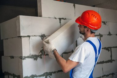 Usta ustabaşı bir ev inşa ederken havalandırmalı beton bloklardan bir duvar örer. Özel konut inşaatı. Havalı beton bloklar inşa etmek için modern teknoloji ve malzemeler.