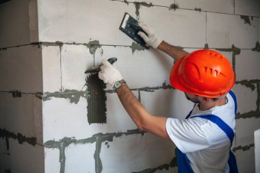 Usta ustabaşı bir ev inşa ederken havalandırmalı beton bloklardan bir duvar örer. Özel konut inşaatı. Havalı beton bloklar inşa etmek için modern teknoloji ve malzemeler.