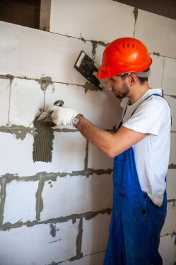Usta ustabaşı bir ev inşa ederken havalandırmalı beton bloklardan bir duvar örer. Özel konut inşaatı. Havalı beton bloklar inşa etmek için modern teknoloji ve malzemeler.