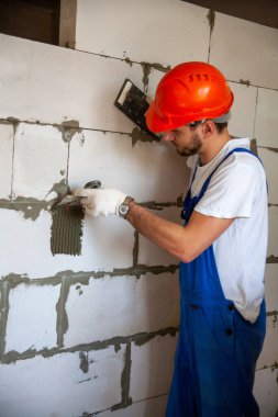 Usta ustabaşı bir ev inşa ederken havalandırmalı beton bloklardan bir duvar örer. Özel konut inşaatı. Havalı beton bloklar inşa etmek için modern teknoloji ve malzemeler.