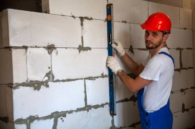 Usta ustabaşı bir ev inşa ederken havalandırmalı beton bloklardan bir duvar örer. Özel konut inşaatı. Havalı beton bloklar inşa etmek için modern teknoloji ve malzemeler.