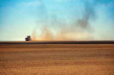 Kırsal arkaplan - küçük bir traktör ufukta toz bulutları içinde geniş bir arazi tarlası sürüyor
