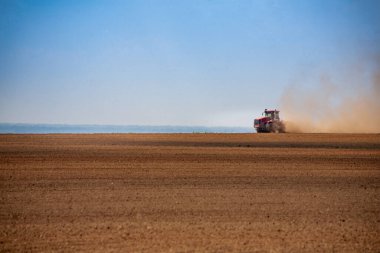 Kırsal arkaplan - küçük bir traktör ufukta toz bulutları içinde geniş bir arazi tarlası sürüyor