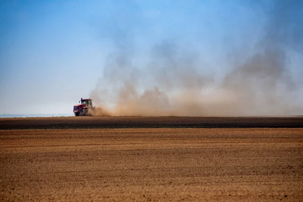 Kırsal arkaplan - küçük bir traktör ufukta toz bulutları içinde geniş bir arazi tarlası sürüyor