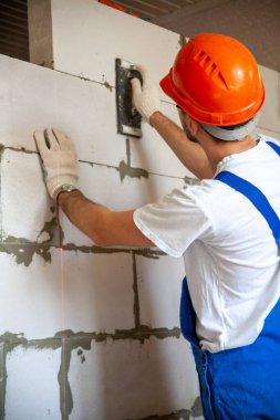 Mason, inşa edilmiş ev duvarının havalandırmalı beton bloğunu hizalıyor.