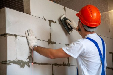 Mason, inşa edilmiş ev duvarının havalandırmalı beton bloğunu hizalıyor.