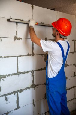 Mason, inşa edilmiş ev duvarının havalandırmalı beton bloğunu hizalıyor.