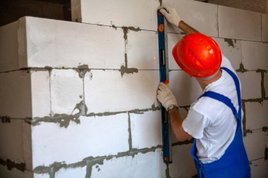 Mason, inşa edilmiş ev duvarının havalandırmalı beton bloğunu hizalıyor.