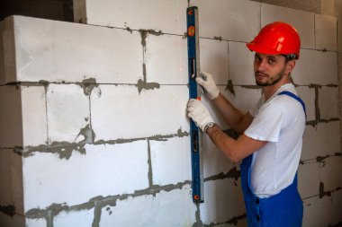 Mason, inşa edilmiş ev duvarının havalandırmalı beton bloğunu hizalıyor.