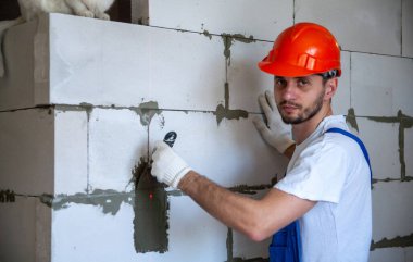 Mason, inşa edilmiş ev duvarının havalandırmalı beton bloğunu hizalıyor.