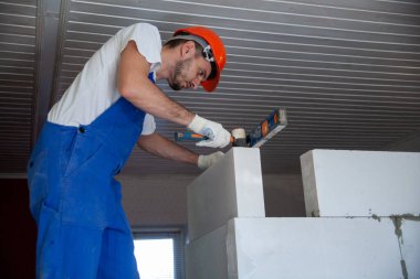 Mason, inşa edilmiş ev duvarının havalandırmalı beton bloğunu hizalıyor.