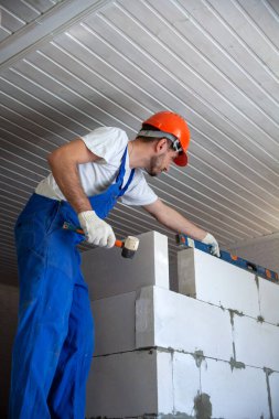 Mason, inşa edilmiş ev duvarının havalandırmalı beton bloğunu hizalıyor.