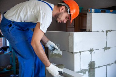 Mason, inşa edilmiş ev duvarının havalandırmalı beton bloğunu hizalıyor.