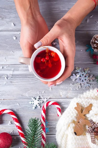 Mains d'une fille tenant une tasse de thé chaud contre une table en bois gris décorée de jouets de Noël avec un espace de copie. Vue du dessus — Photo