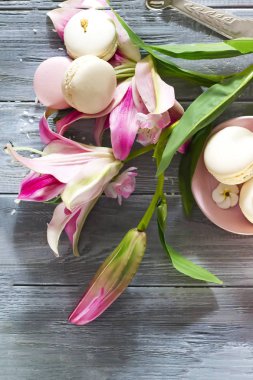 Kopya alanı ile gri ahşap arka plan üzerinde pembe zambak çiçek ile Geleneksel Fransız macaroon çerezleri. Düz yatıyordu