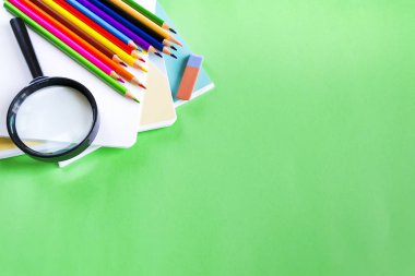 Kalemler, silgiler, defterler, yeşil arka plan üzerinde büyüteç ve metin için kopya alanı. Okul ve eğitim