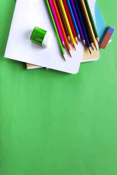 Різнокольорові олівці, блокноти, гумка і точилка на зеленому тлі з пробілом для тексту. Шкільний набір. Плоский прошарок — стокове фото