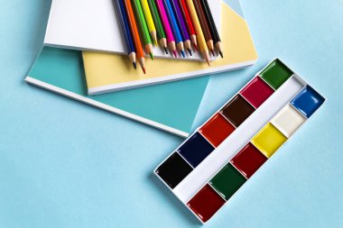 Kopya alanı ile mavi bir arka plan üzerinde defter, renkli kalem ve suluboya Okul seti. Üstte görüntü