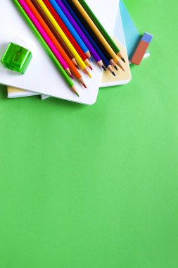 Metin alanı ile yeşil bir arka planda çok renkli kalemler, dizüstü bilgisayarlar, silgi ve kalemince. Okul Seti. Düz yatma
