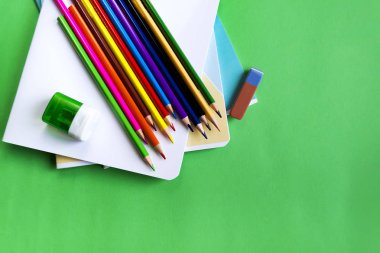 Okul defteri seti, kalem, kopya alanı ile yeşil bir arka planda bir silgi ve kalemtırlar.