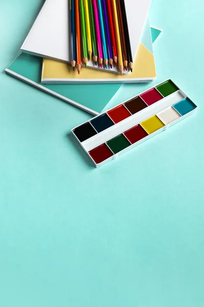 Шкільний набір зошитів, кольорові олівці та акварелі на синьому фоні з копіювальним простором. Вид зверху — стокове фото