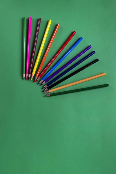 Набір різнокольорових дерев'яних олівців на зеленому паперовому фоні з копіювальним простором. Шкільний аксесуар. Плоский прошарок — стокове фото