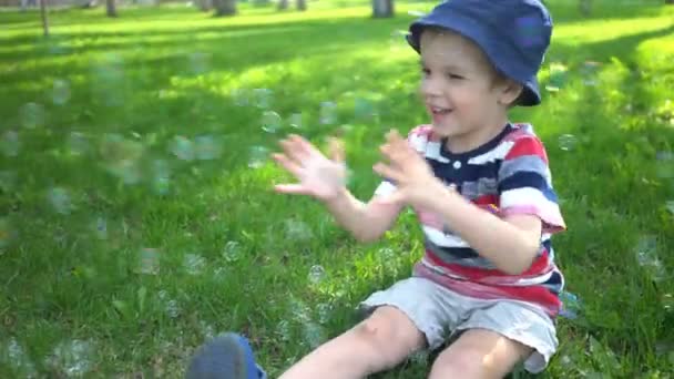 Feliz niño soplando burbujas de jabón en el parque — Vídeo de stock