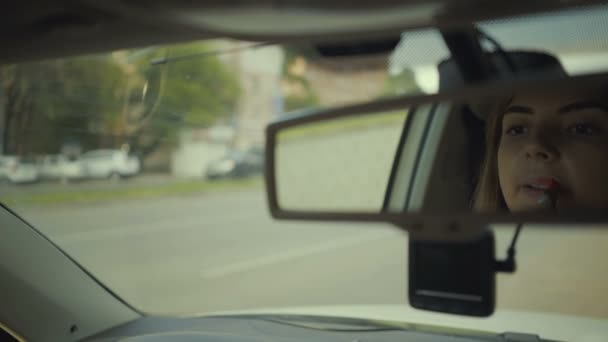 Mladá dívka namaluje rty v autě v odrazu v zrcadle — Stock video