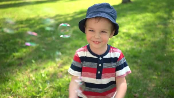 Šťastný chlapec fouká mýdlové bubliny v parku — Stock video