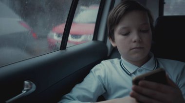 Sosyal ağ üstünde onun smartphone kullanarak yağmurlu gün boyunca şehirde Araba sürme üzgün, mutsuz genç çocuk