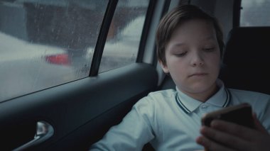 Sosyal ağ üstünde onun smartphone kullanarak yağmurlu gün boyunca şehirde Araba sürme üzgün, mutsuz genç çocuk