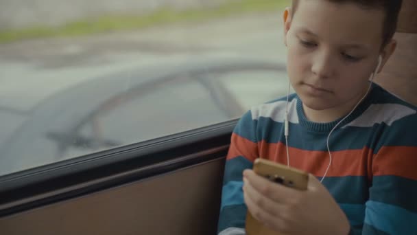 特写镜头, 一个年轻的男孩乘公交车穿过城市。他在智能手机上使用社交网络, 听音乐. — 图库视频影像