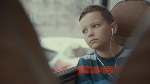 特写镜头, 一个年轻的男孩乘公交车穿过城市。他听音乐. — 图库视频影像