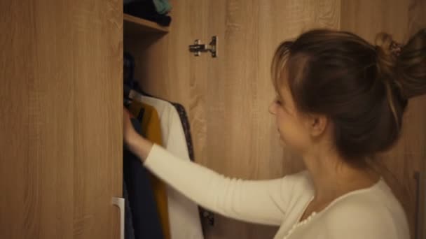 Kvinna att välja klänning från skåpet i rummet. Attraktiv dam med brunt hår ser ut för att besluta vad man ska ha. — Stockvideo