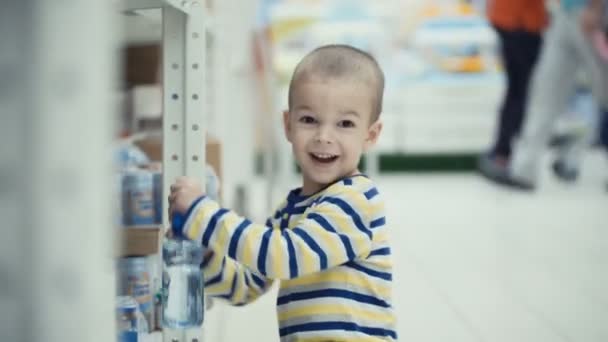 Mały chłopiec w supermarkecie wybierz polecenie butelką wody mineralnej. — Wideo stockowe