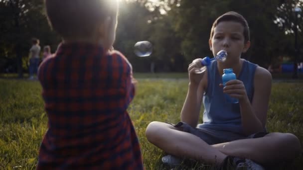 Two boys blowing soap bubbles outdoors summer. — Stock Video