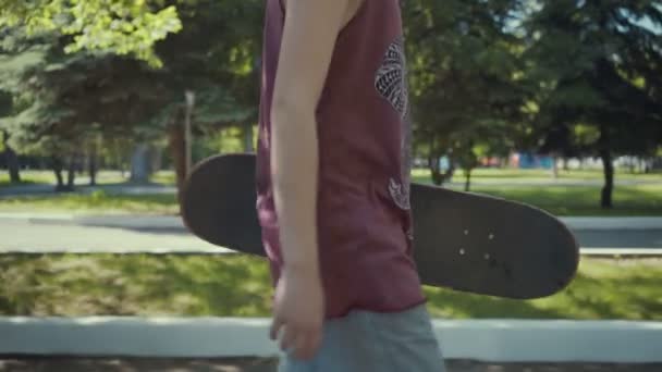 Skateboarder βόλτες σε ένα πάρκο με ένα skateboard στα χέρια. — Αρχείο Βίντεο