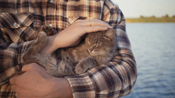 自然湖の近くに猫をなでる若い男. — ストック写真