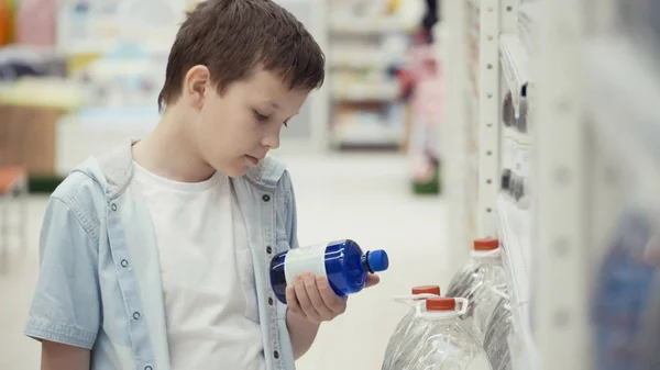 Kisfiú a szupermarketben válasszon egy üveg ásványvíz. — Stock Fotó