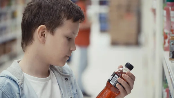 Мальчик в супермаркете выбирает бутылку минеральной воды . — стоковое фото