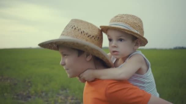 Два брата ходят по полю в соломенных шляпах летом . — стоковое видео