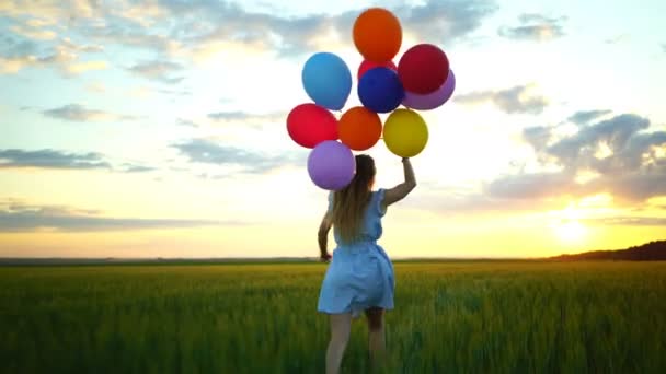 Lycklig kvinna med ballonger som körs i fältet vete vid solnedgången — Stockvideo