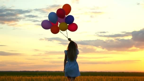 šťastná žena s balóny, které jsou spuštěny v poli pšenice při západu slunce
