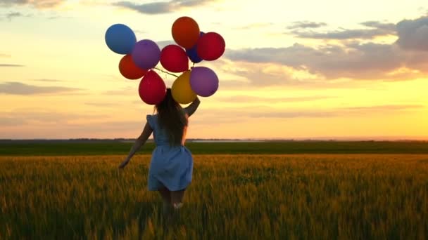 Lycklig kvinna med ballonger som körs i fältet vete vid solnedgången — Stockvideo